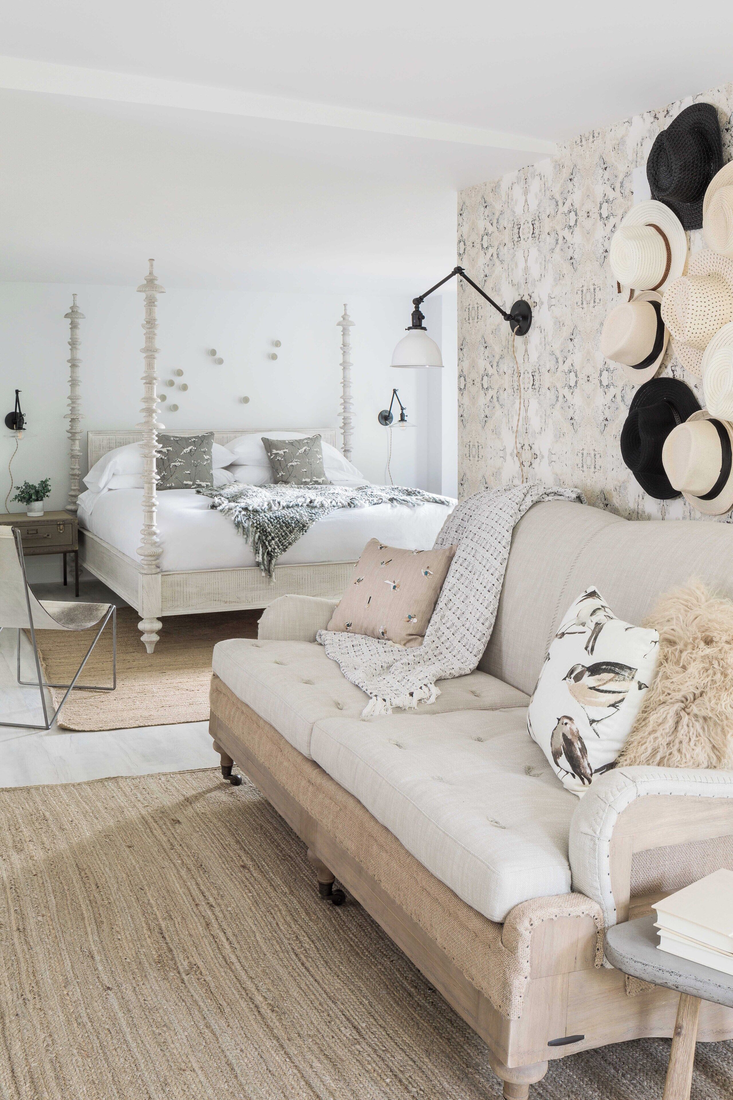 A bedroom with a four-poster bed, a sofa, a small table, and a wall-mounted hat rack.