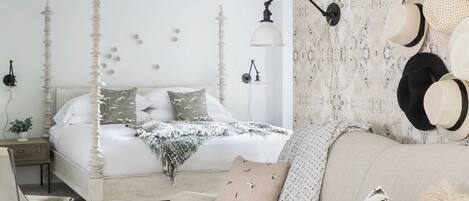 A bedroom with a four-poster bed, a sofa, a small table, and a wall-mounted hat rack.
