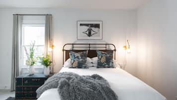 Un dormitorio con cama, ventana con cortinas, un cuadro en la pared y lámparas de noche.