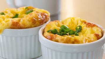 Two white ramekins with a baked dish, garnished with green onions, on a white plate with a fork.