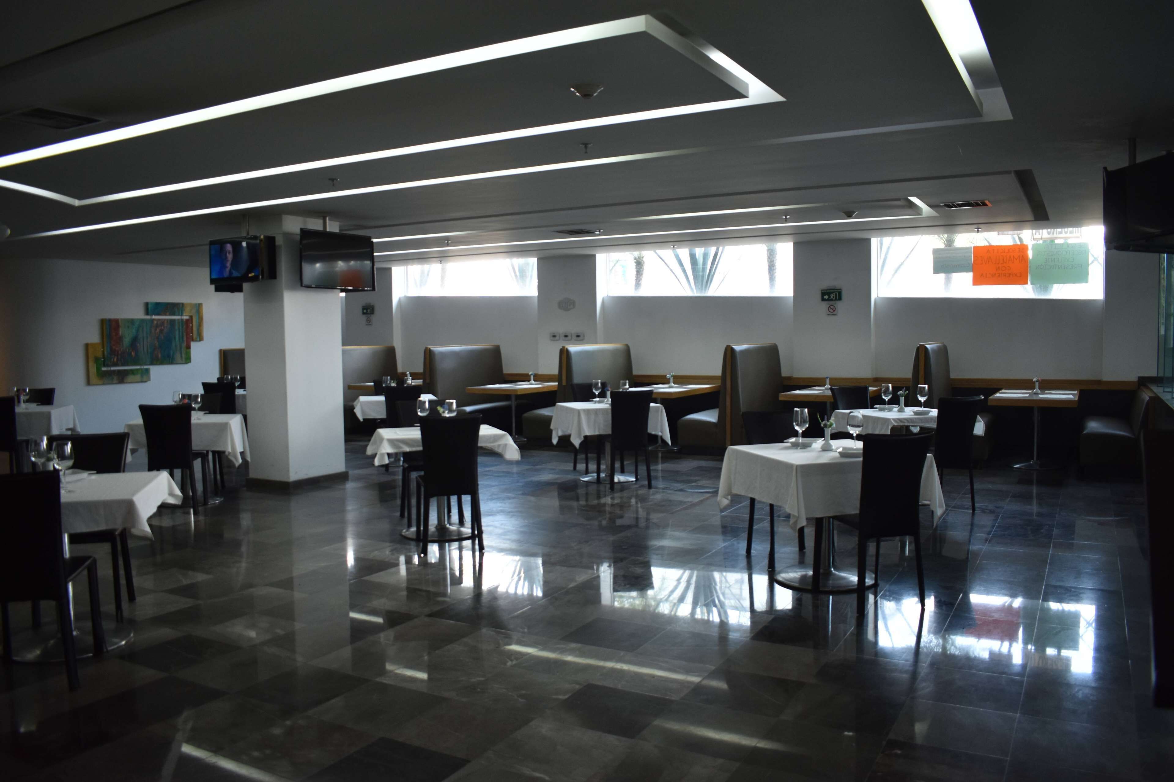Un restaurante con una decoración moderna, que ofrece una combinación de asientos tipo cabina y mesas, piso de baldosas y un televisor de pantalla plana montado en la pared.