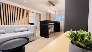 A modern living room with a grey sofa, a black coffee table, a wooden slatted wall, a dining area with a black table, and a potted plant. - Ramada by Wyndham Mexico City Santa Fe (Mexico City)