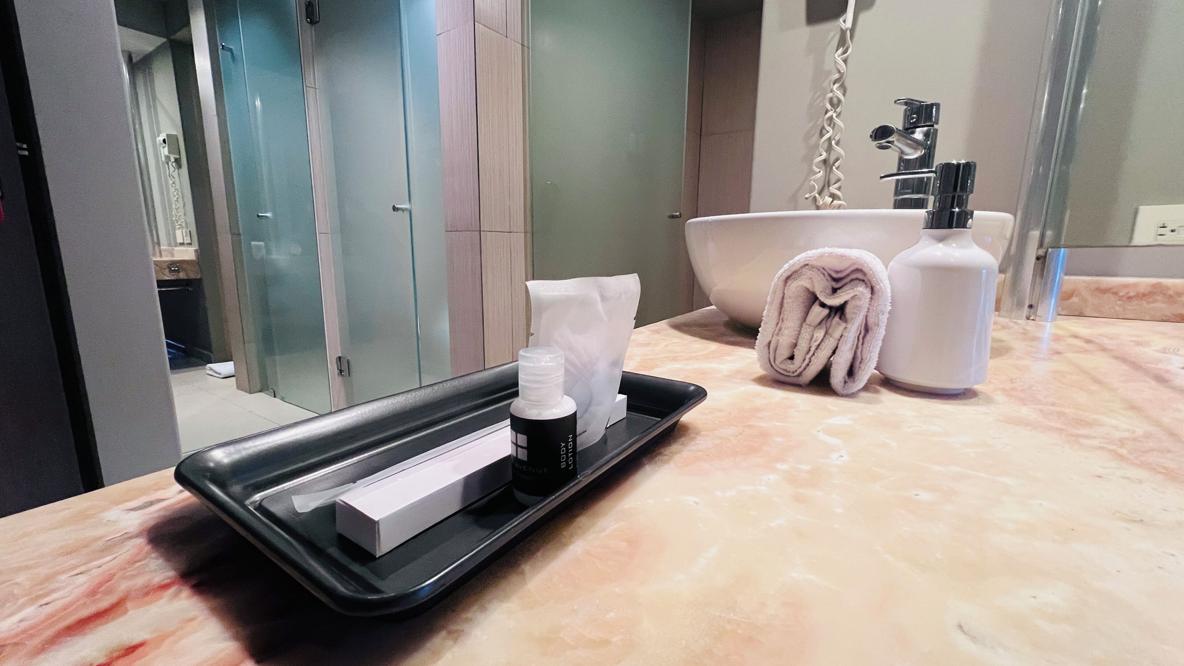 A bathroom with a marble countertop, a sink, a towel, a bottle of lotion, and a tray with a box and a bottle.