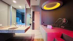 A modern bathroom with a large mirror, a vanity with a marble countertop, a red accent wall, and a circular light fixture. - Ramada by Wyndham Mexico City Santa Fe (Mexico City)