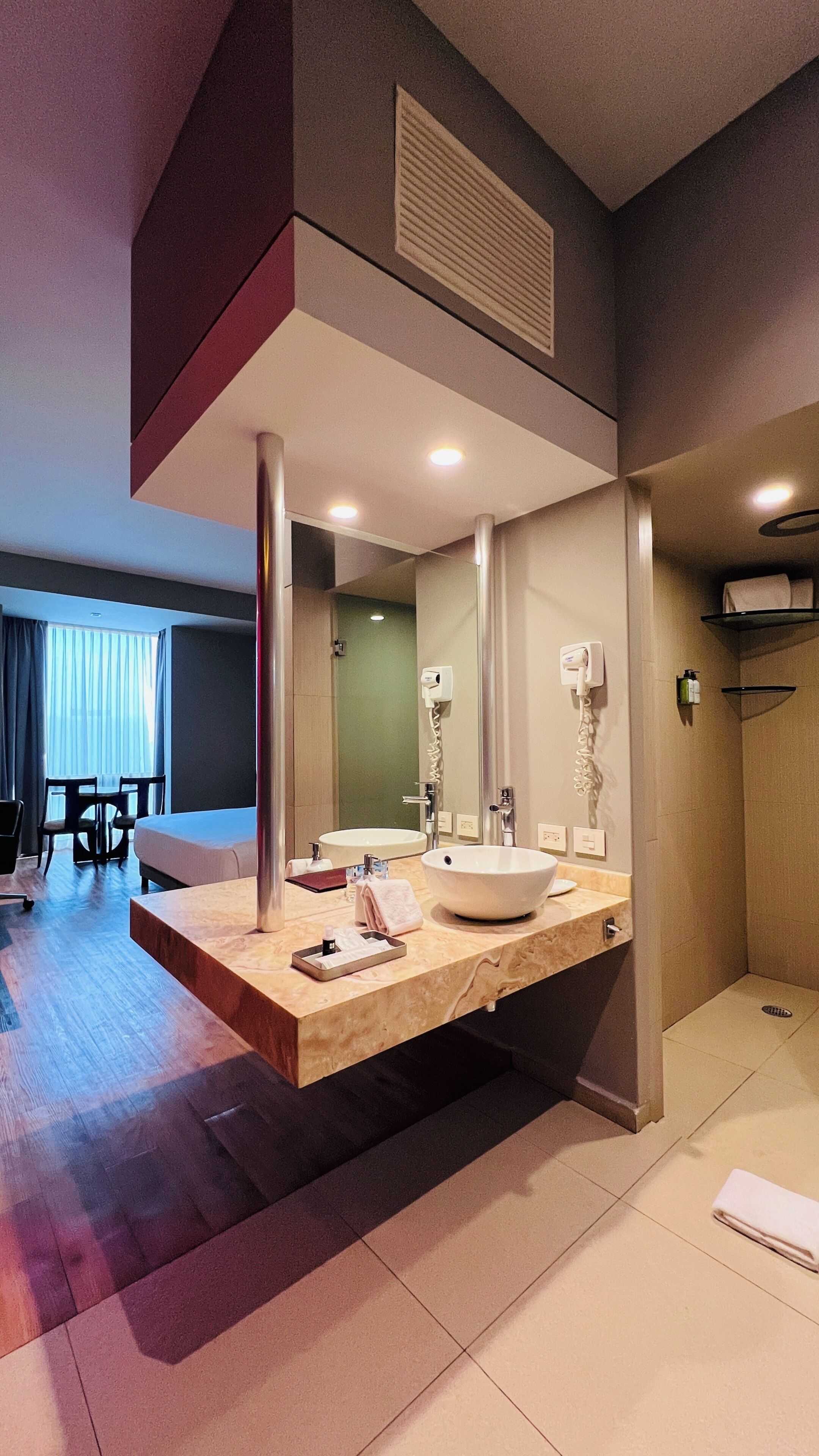 A modern bathroom with a large mirror, two sinks, a shower area, and a seating area with a table and chairs.