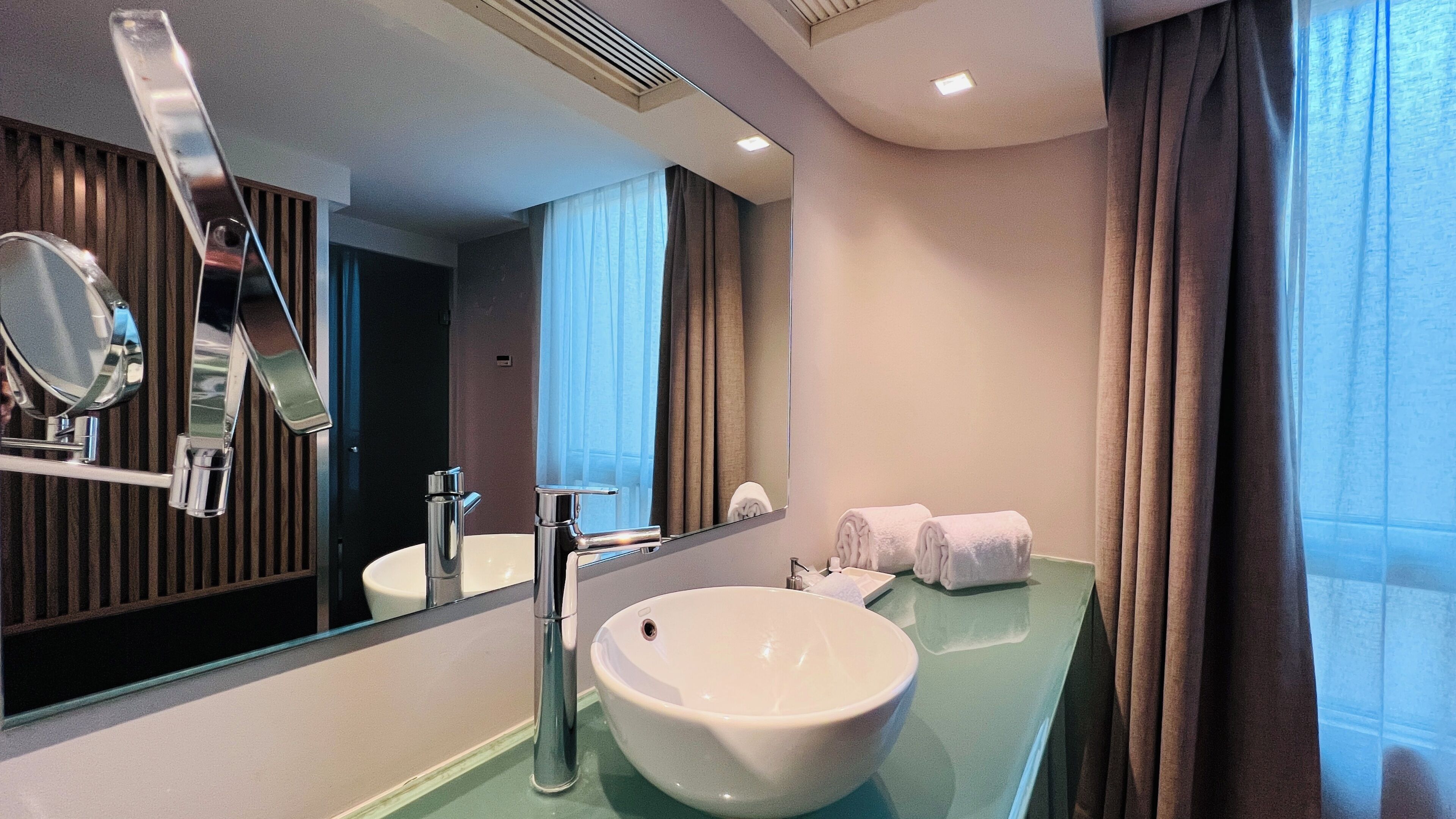 A modern bathroom with a large mirror, a white sink, and a towel rack.