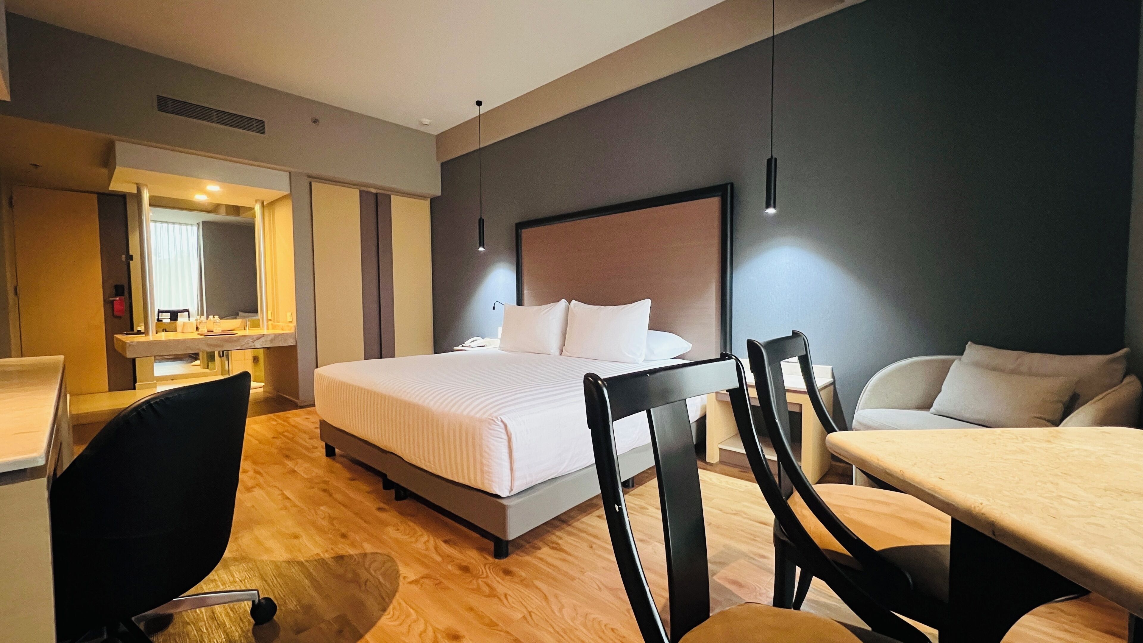 Hotellihuone, jossa on sänky, työpöytä, tuoli, sohva ja peili.