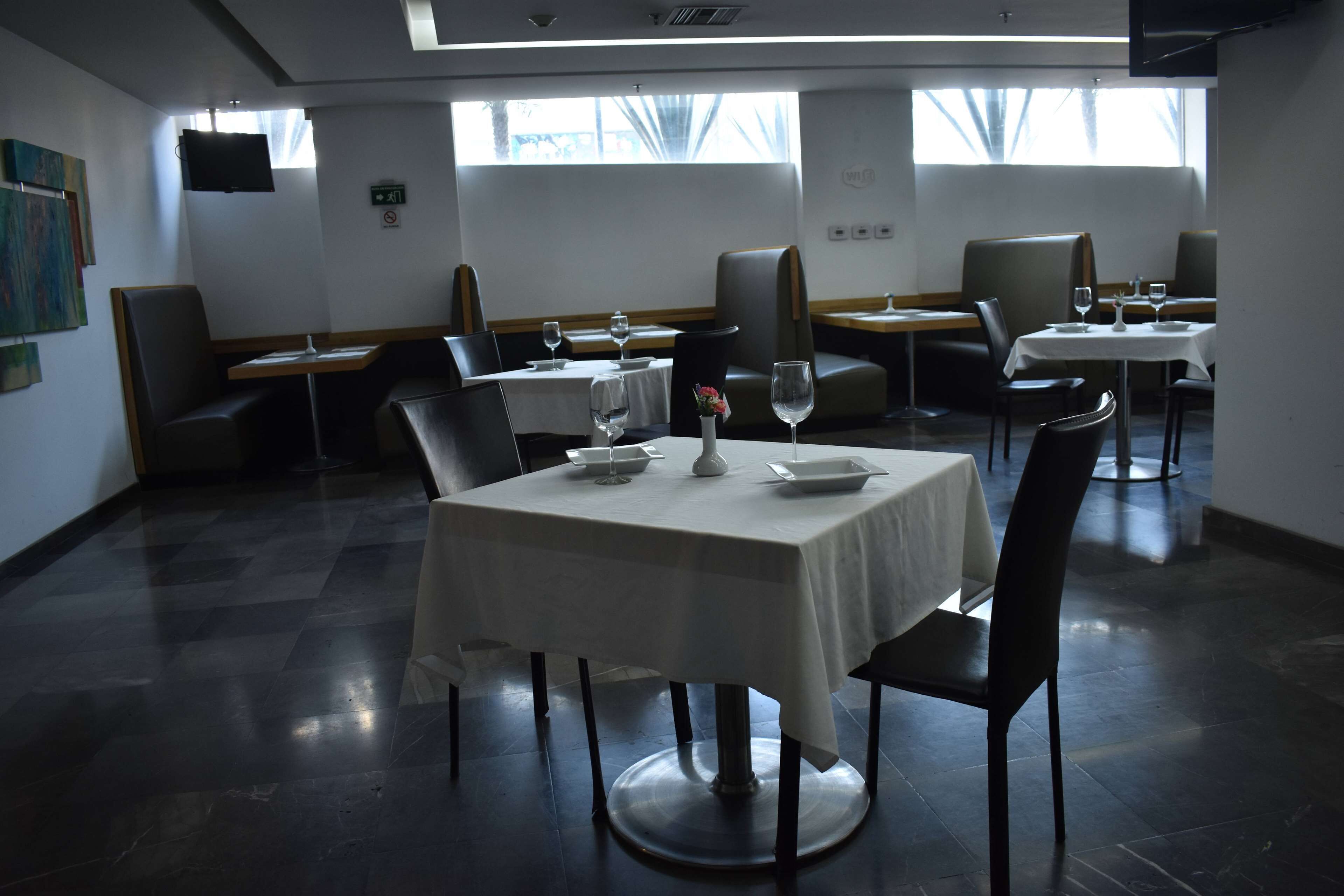 Un restaurant avec des tables dressées pour le service, des chaises et un téléviseur accroché au mur.