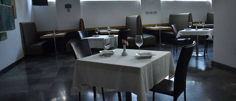 A restaurant with tables set for dining, chairs, and a TV on the wall.