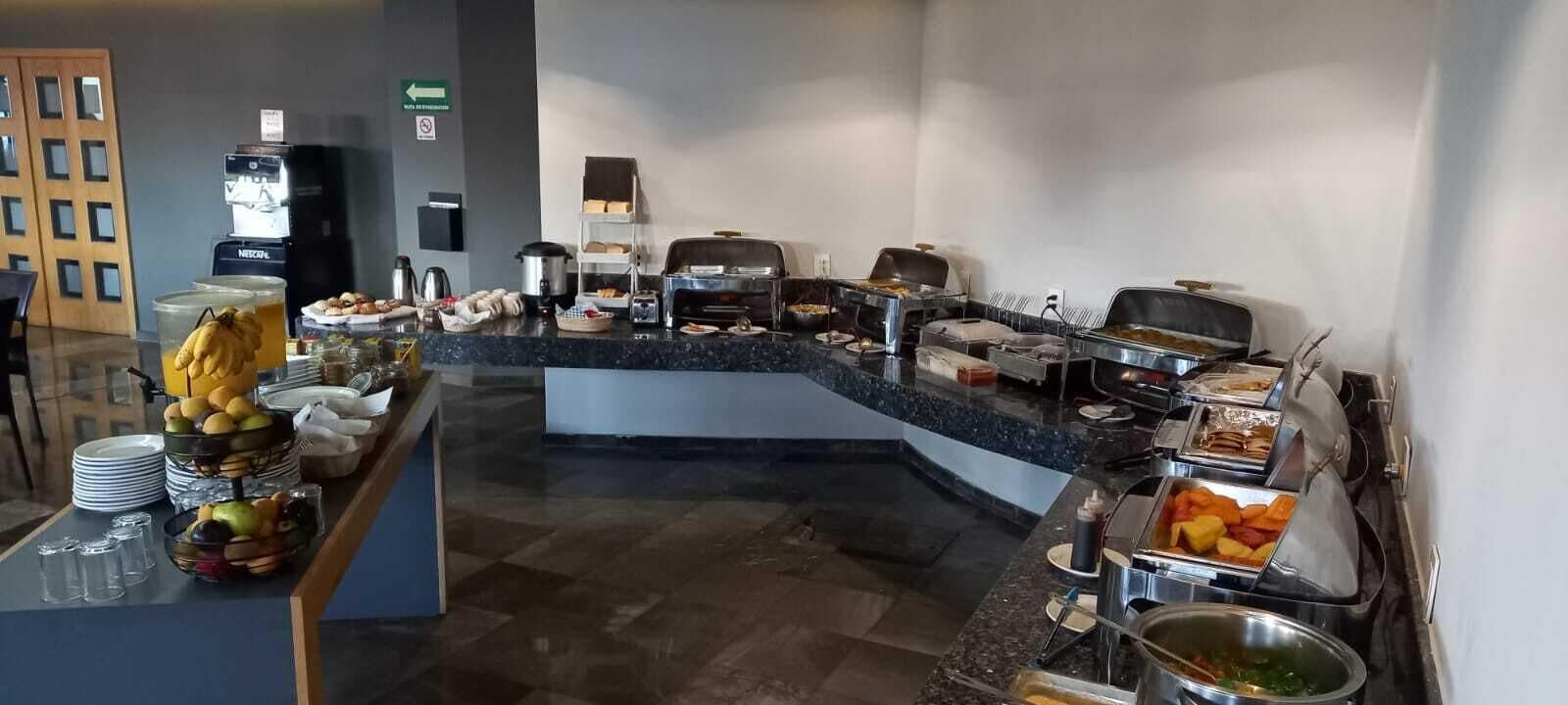 A buffet area with various food stations, including a fruit bowl, a coffee machine, and multiple serving trays.