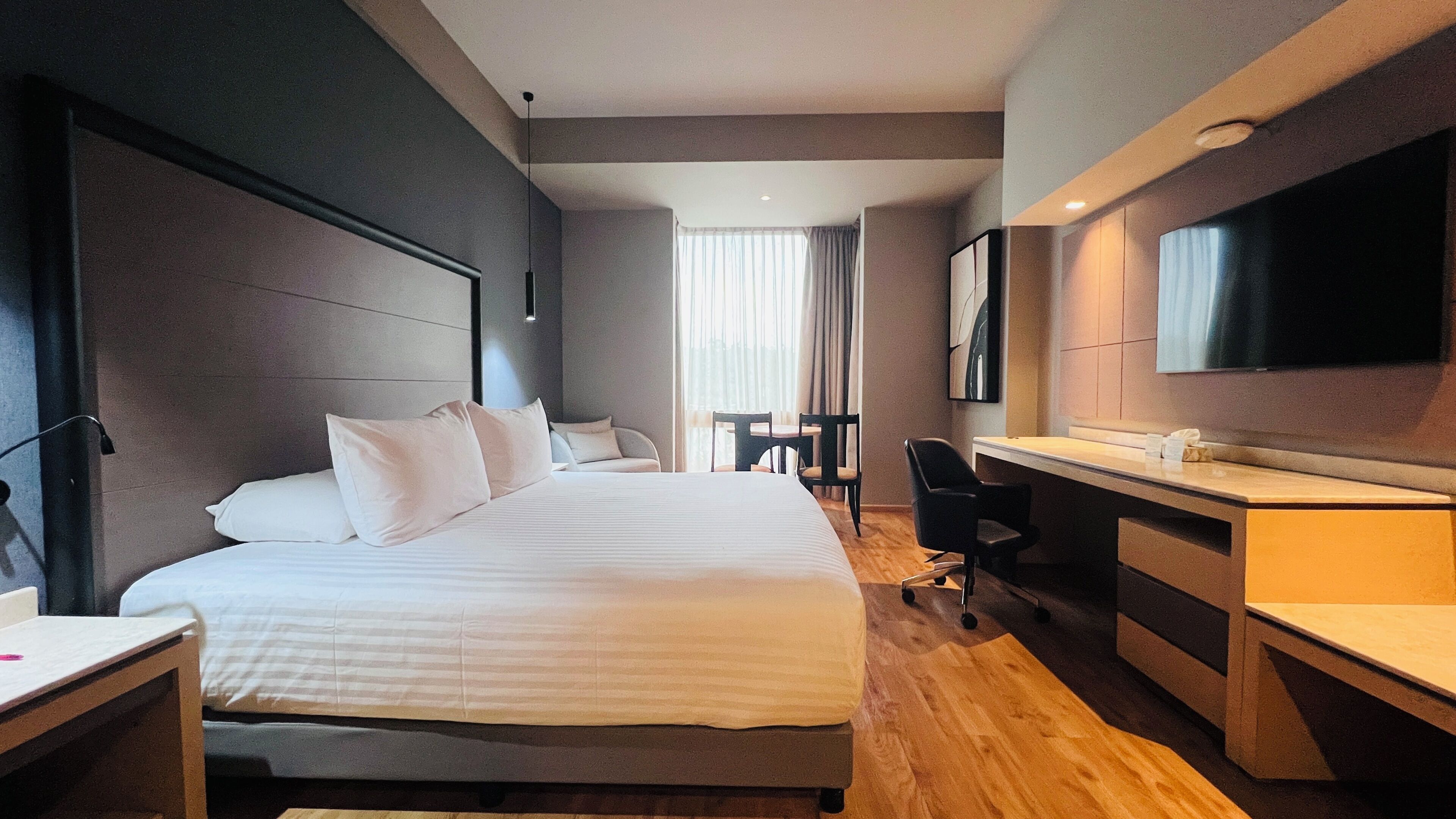 A hotel room with a bed, desk, chair, and a TV mounted on the wall.