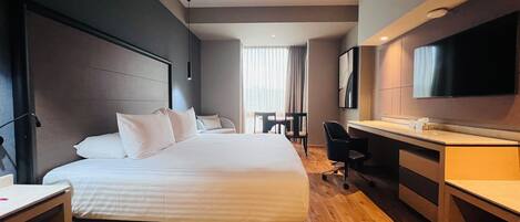 A hotel room with a bed, desk, chair, and a TV mounted on the wall.