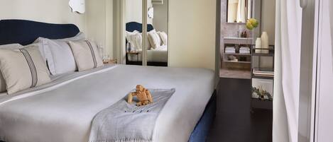 A modern hotel room with a large bed, a wooden nightstand, a mirror, and a bathroom with a vanity and shelves.