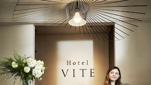 Un mostrador de recepción de hotel con diseño moderno, un cartel que dice "Hotel VITE" y un jarrón con flores.