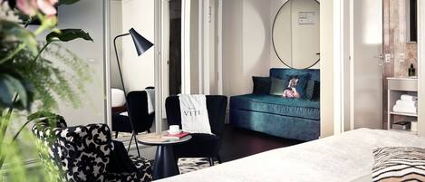 A modern hotel room with a bed, a desk, a chair, a sofa, and a large mirror.
