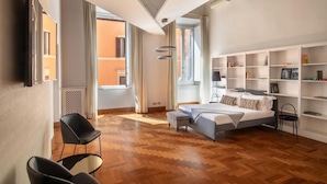 Un dormitorio moderno con cama, zona de estar con sillas, estantería y vistas al exterior.
