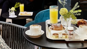Un comedor con una mesa preparada para el desayuno, que incluye un croissant, un vaso de zumo de naranja y un pequeño florero con flores.