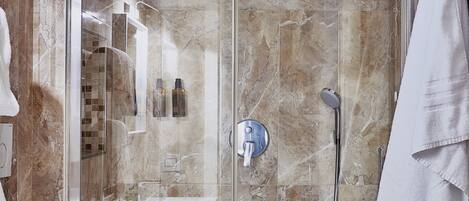 A modern bathroom with a glass-enclosed shower, marble walls, a toilet, and a towel rack.