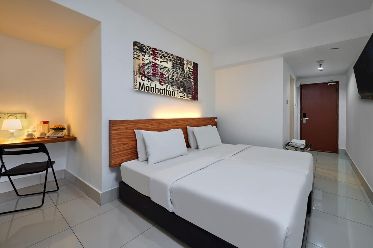 A hotel room with a bed, a desk with a lamp, a telephone, and a painting on the wall.