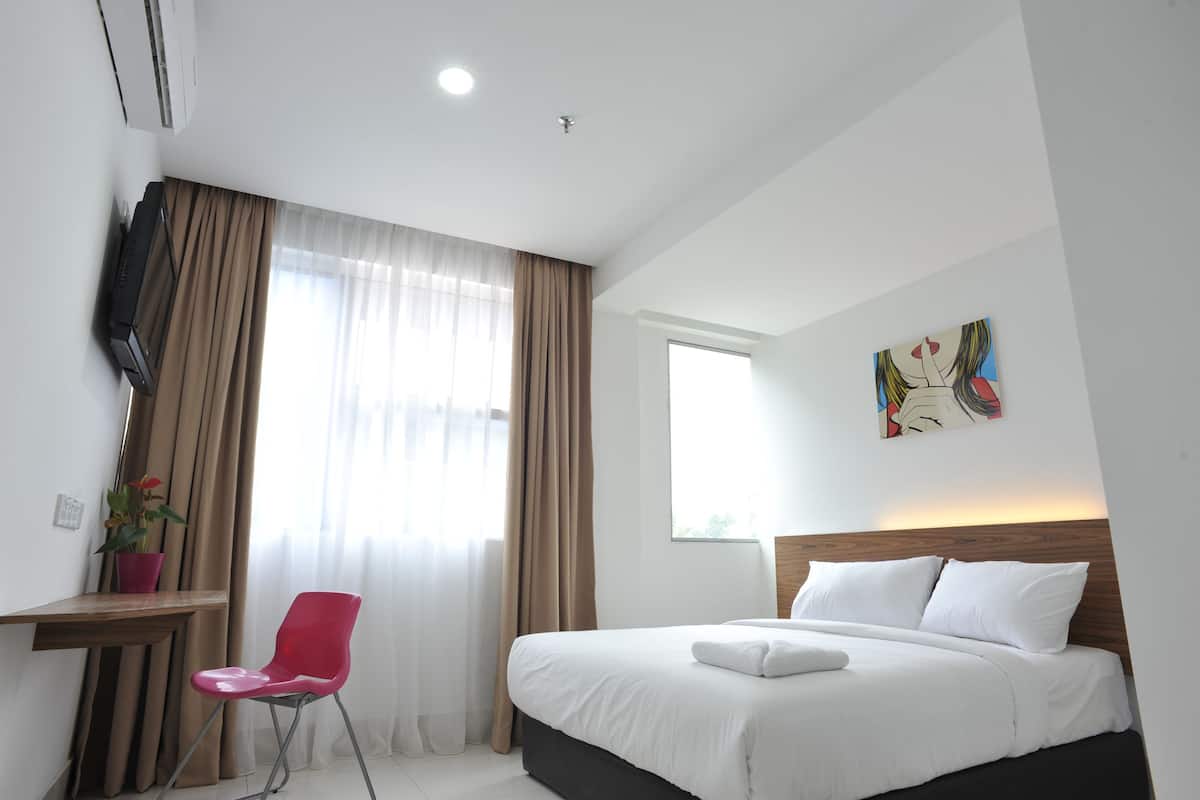 A hotel room with a bed, a desk, a chair, a TV, and a window with curtains.