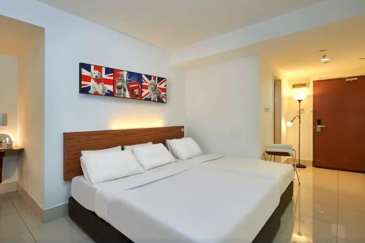 A hotel room with a large bed, a desk with a lamp, and a wall with a flag-themed artwork.