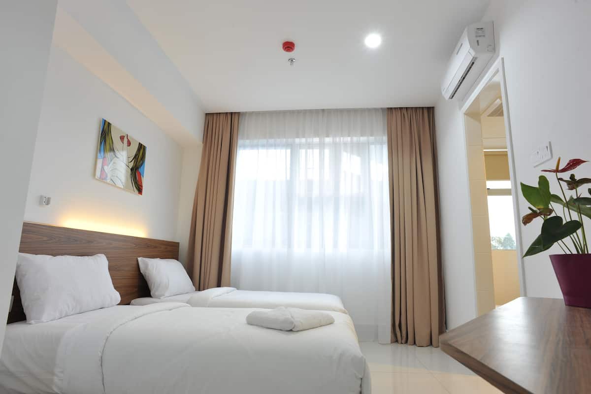A hotel room with two beds, a large window with curtains, a ceiling light, an air conditioning unit, and a potted plant.