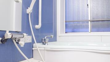 A bathroom with a bathtub, a toilet, and a window with frosted glass.