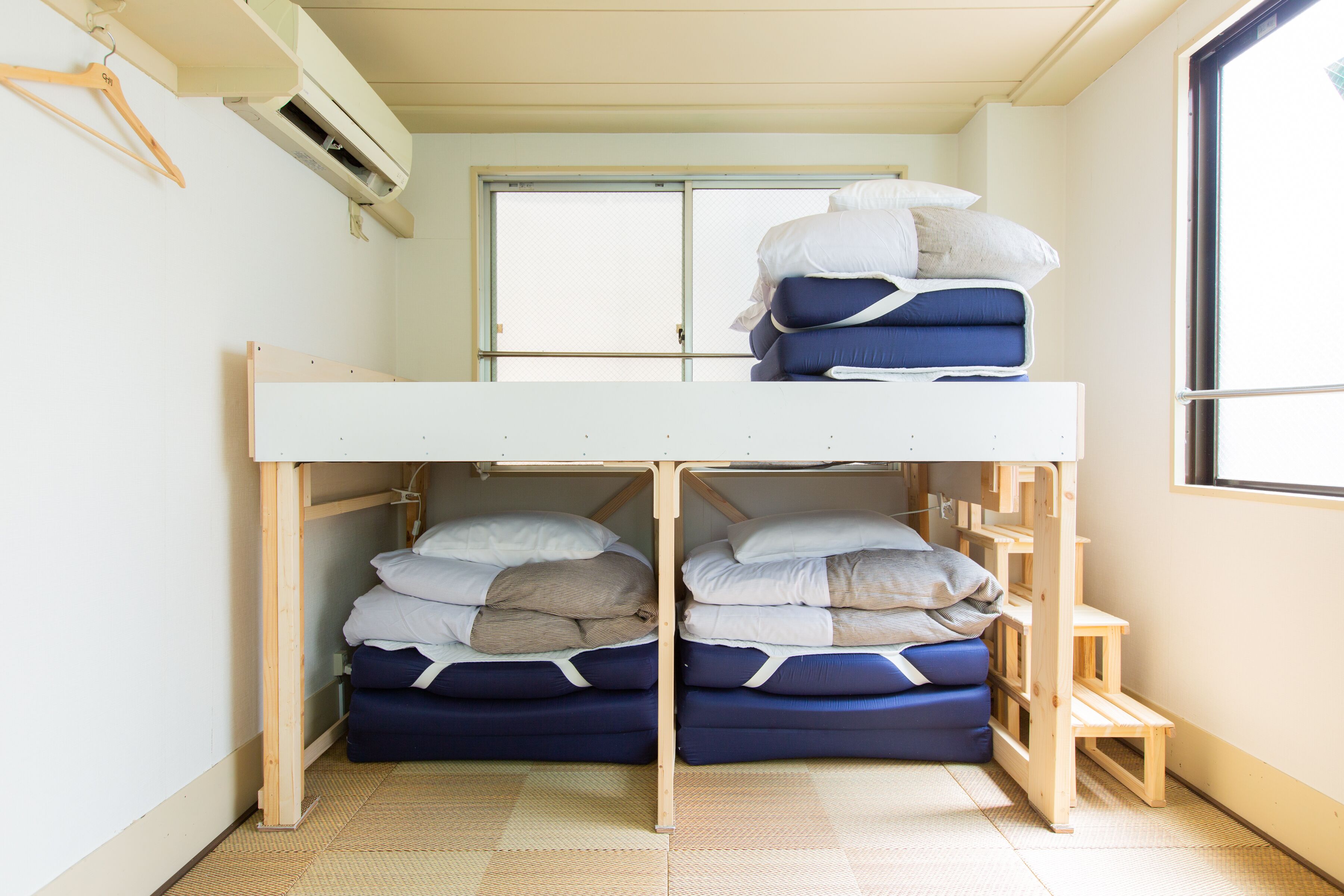 Ein Etagenbett mit zwei Schlafstellen, ein Fenster mit Rollo und ein kleiner Holzschemel.