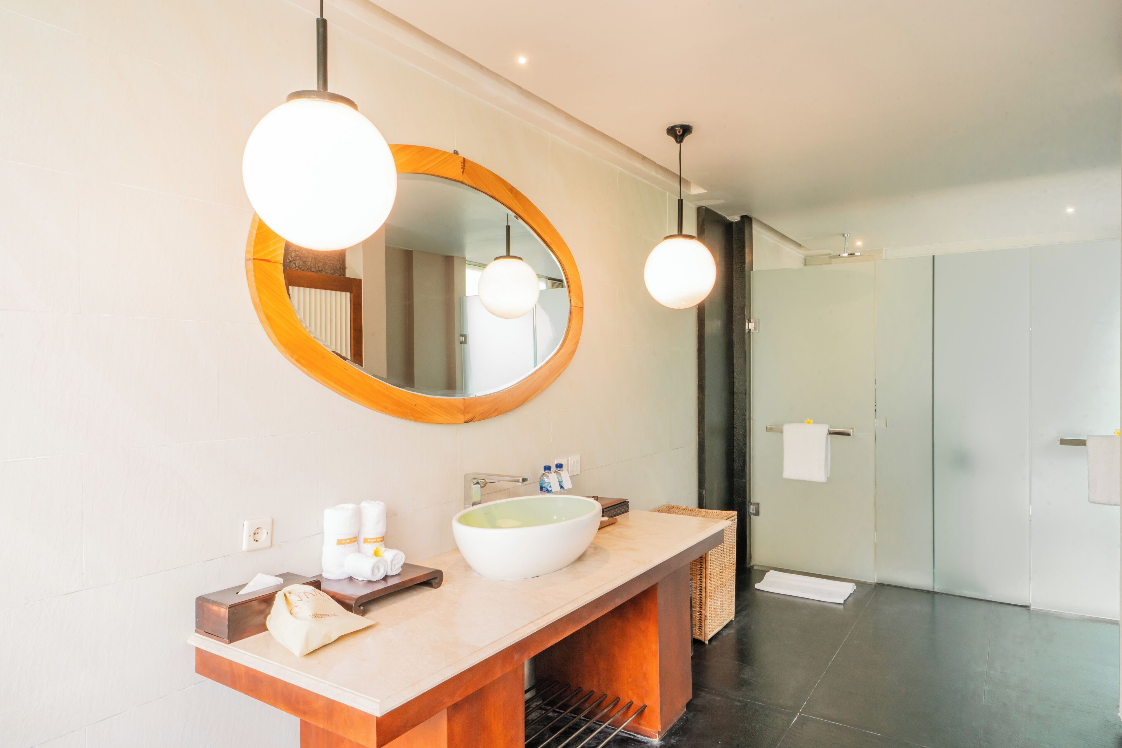 Een moderne badkamer met een grote, ovale spiegel, een witte wastafel en twee hanglampen.