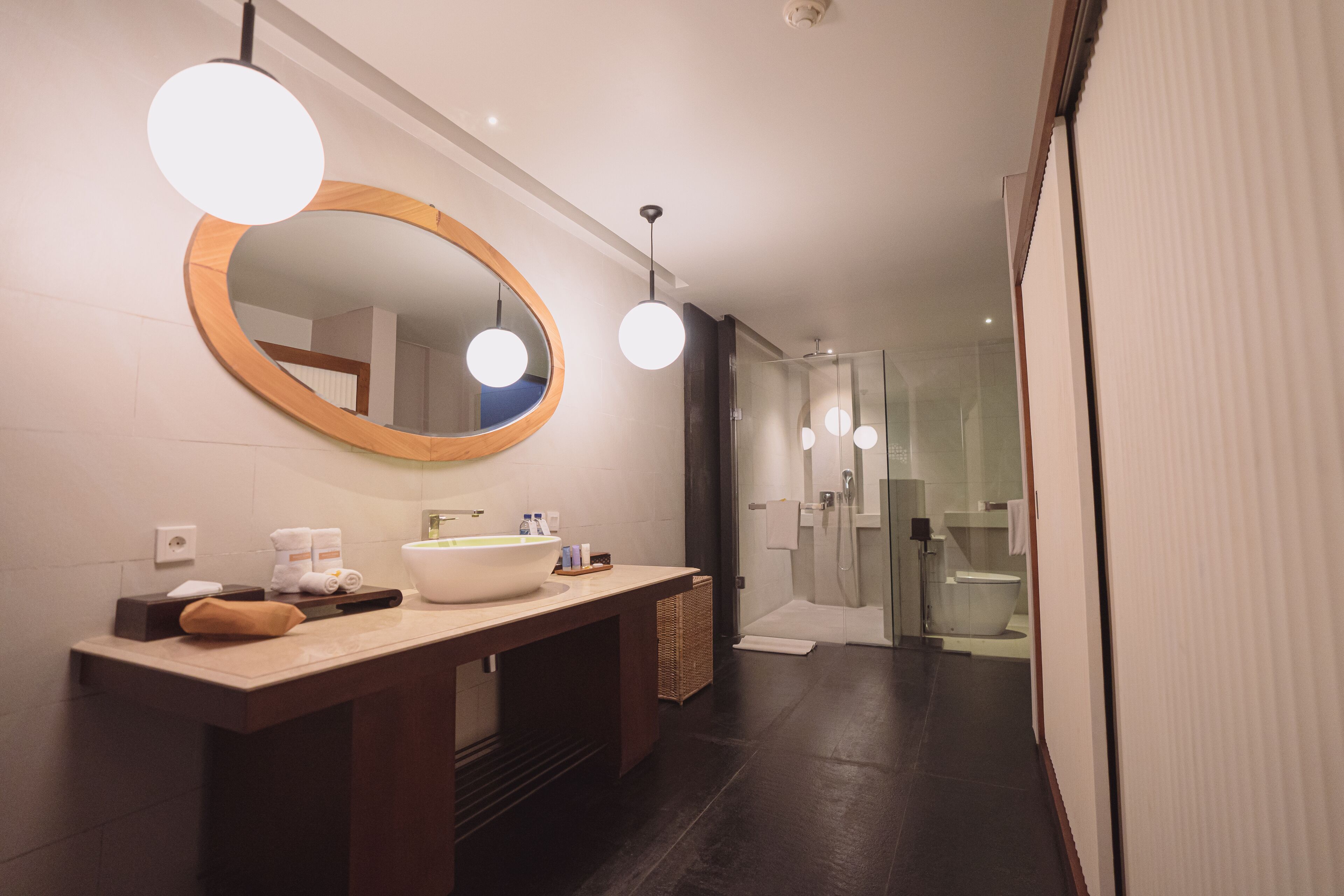 A modern bathroom with a large mirror, a wooden vanity, a large sink, and a glass shower enclosure.