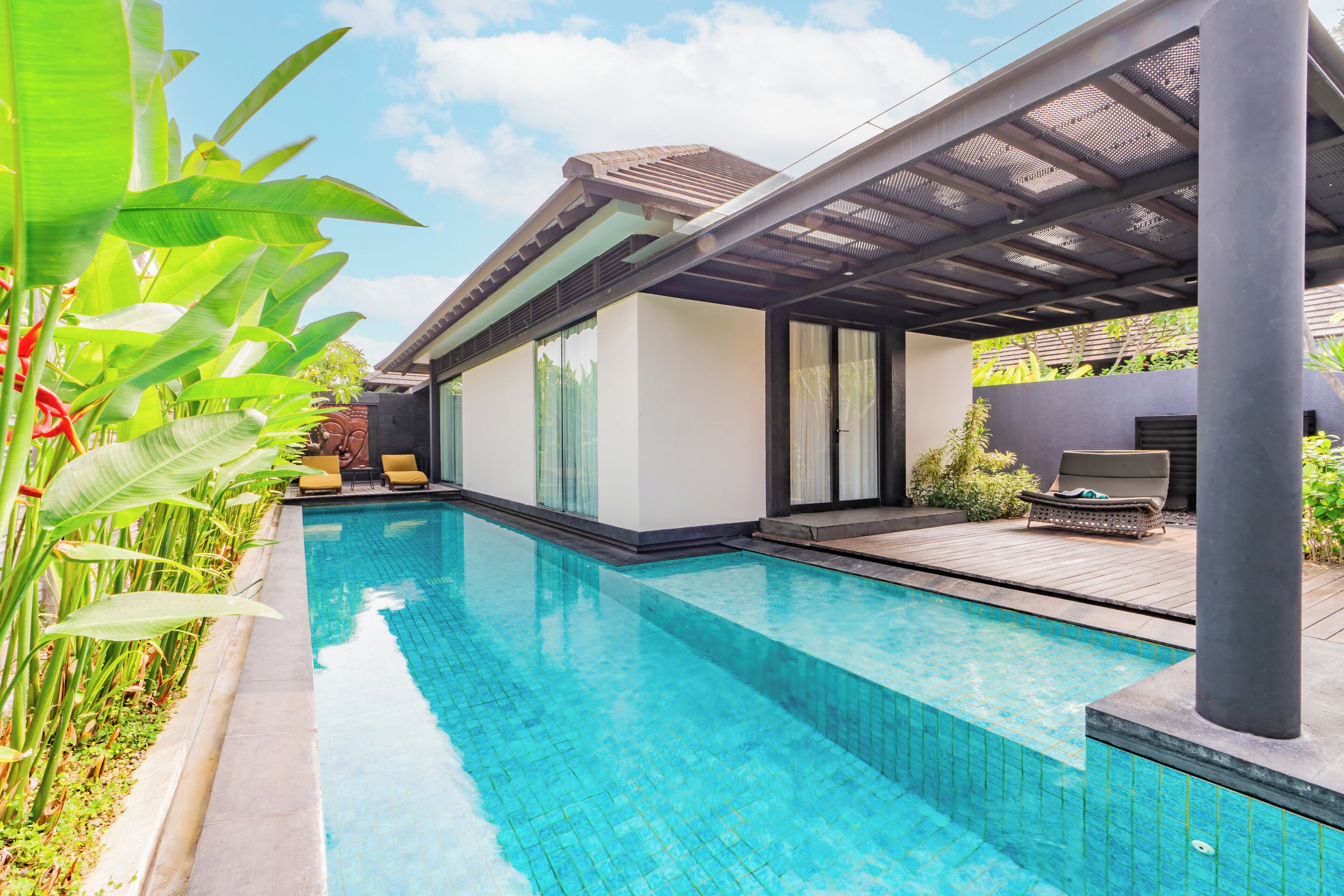 Una piscina con un patio cubierto, rodeada de exuberante vegetación.