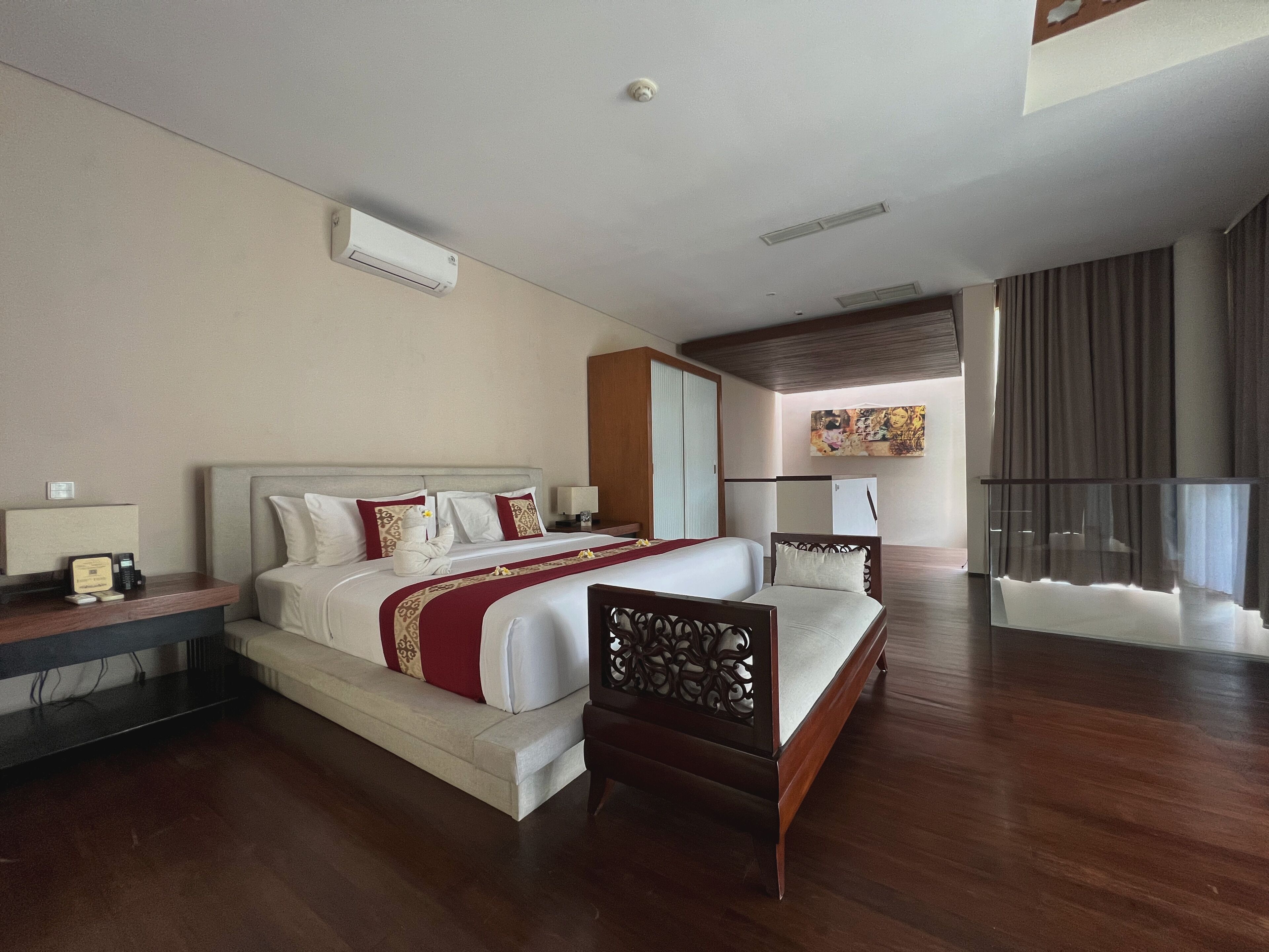 A spacious bedroom with a large bed, a wooden chair, a desk with a telephone, and a painting on the wall.