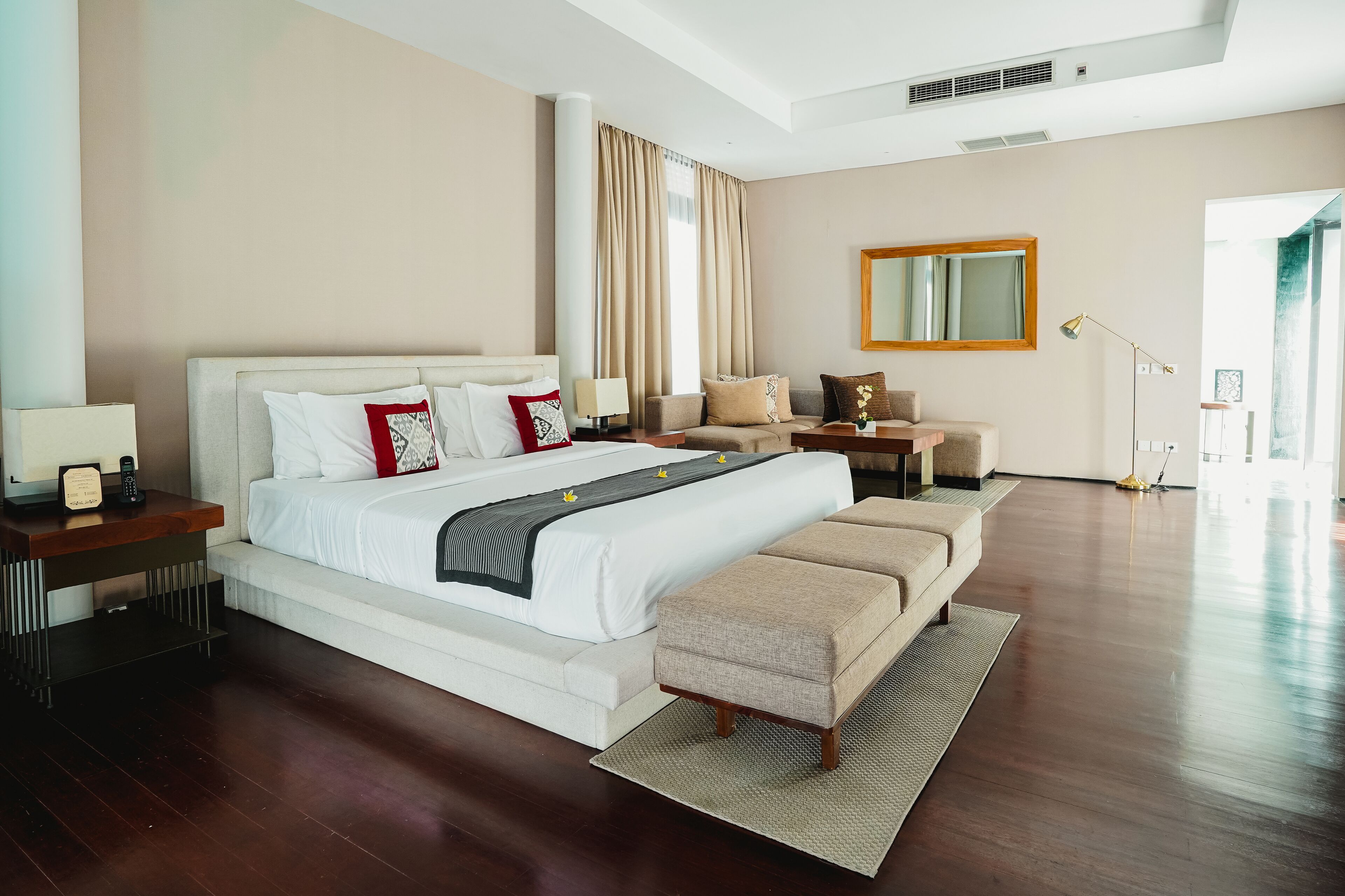 A modern hotel room with a large bed, bedside tables, a sofa, and a mirror.