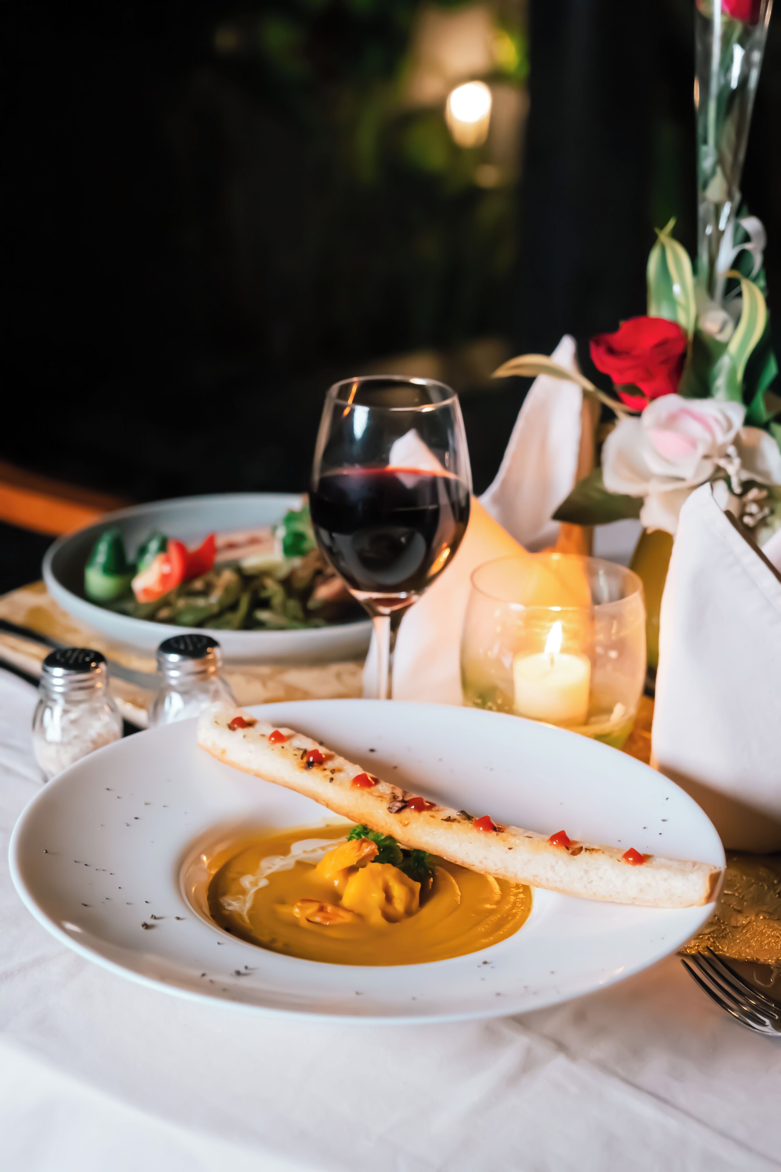 A dining table with a plate of food, a glass of red wine, and a candle.