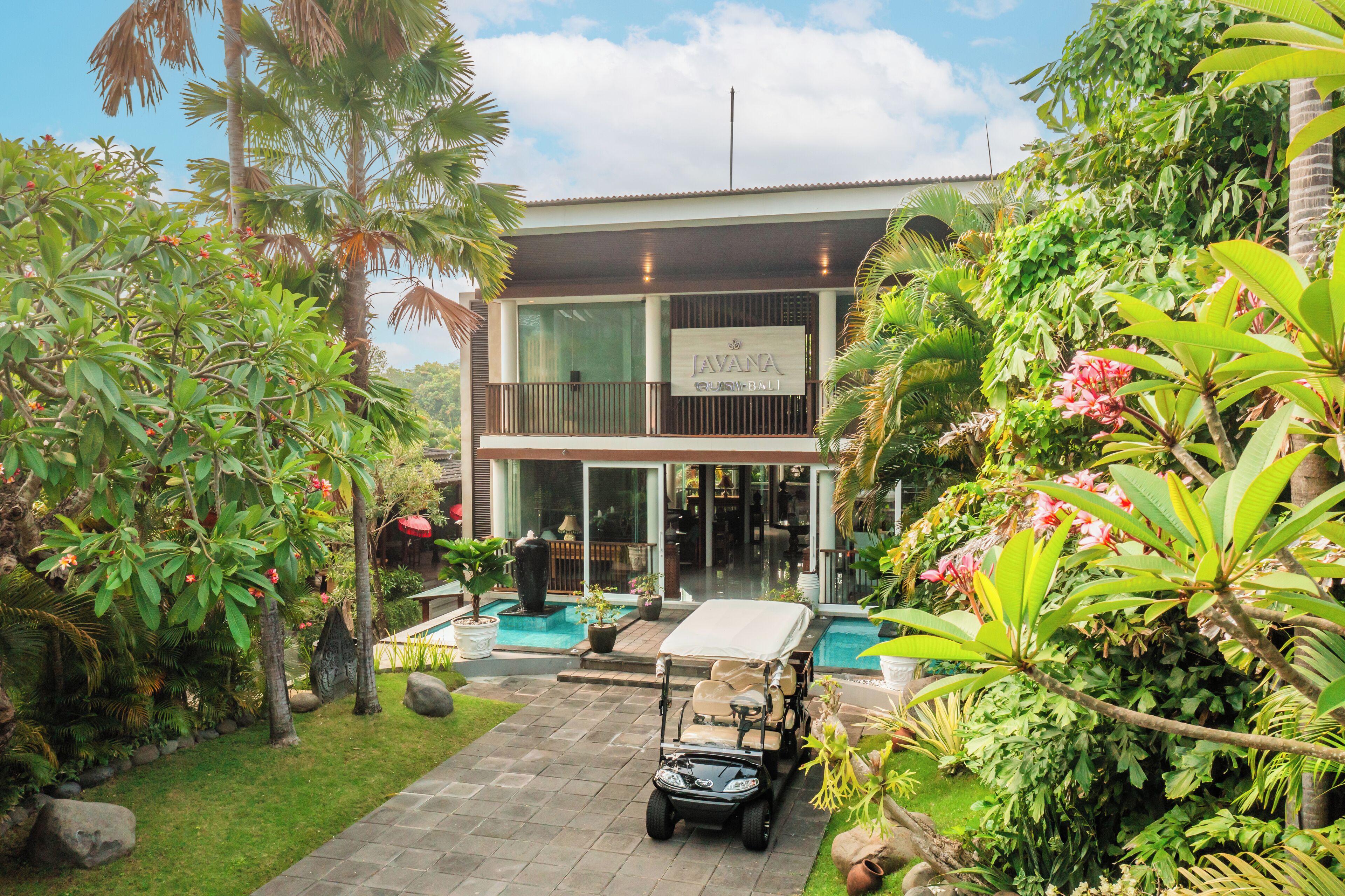 A modern hotel with a pool, lush greenery, and a golf cart.