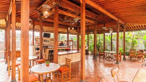 An outdoor covered patio area with wooden tables and chairs, a bar area, and potted plants. - Javana Royal Villas (Keroboken Kelod)