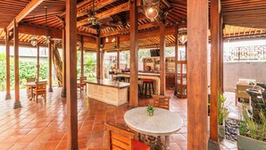 An open-air restaurant with wooden beams, a central bar area, and outdoor seating. - Javana Royal Villas (Keroboken Kelod)