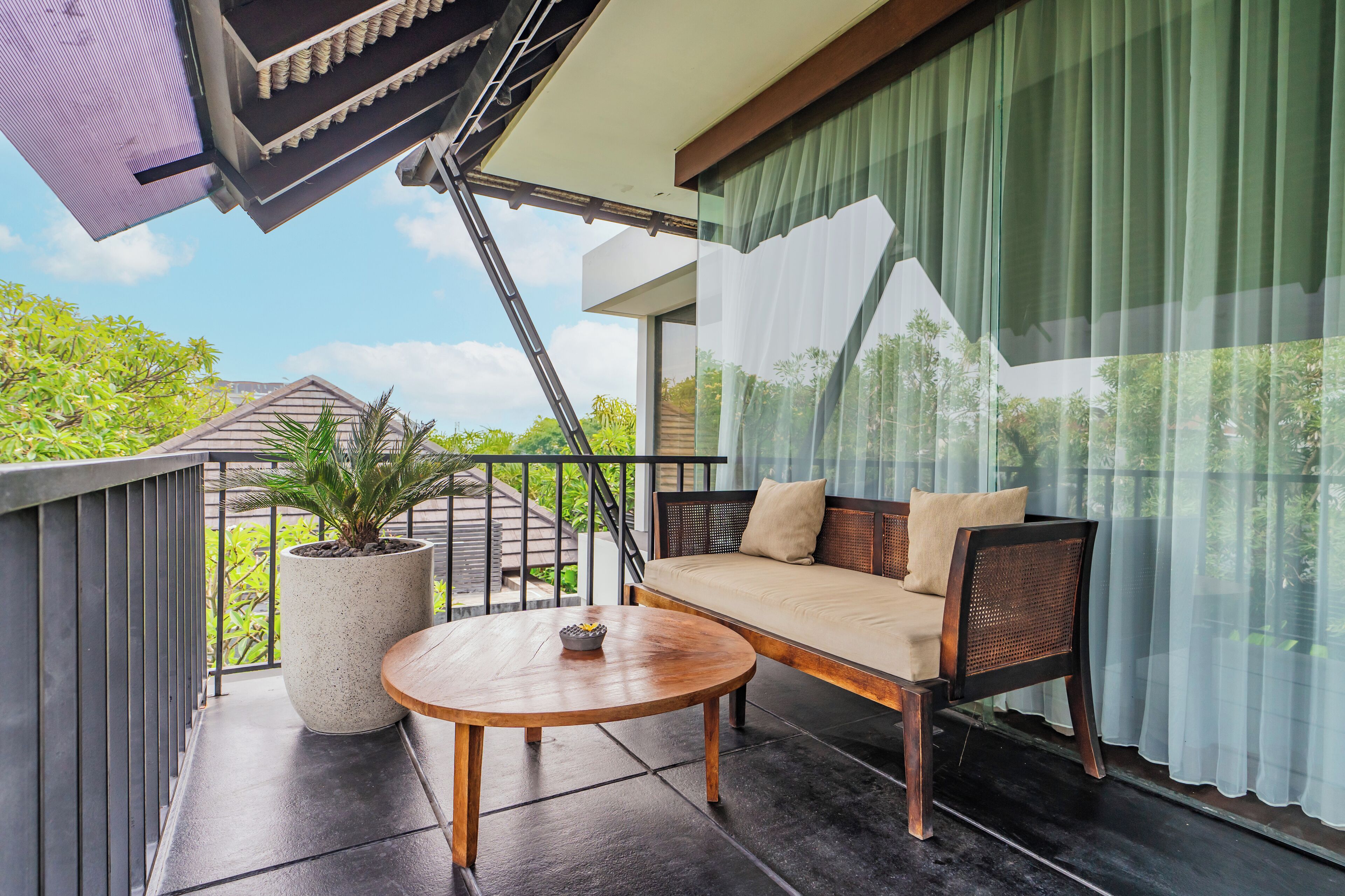 A balcony with a sofa, a round table, and a potted plant.