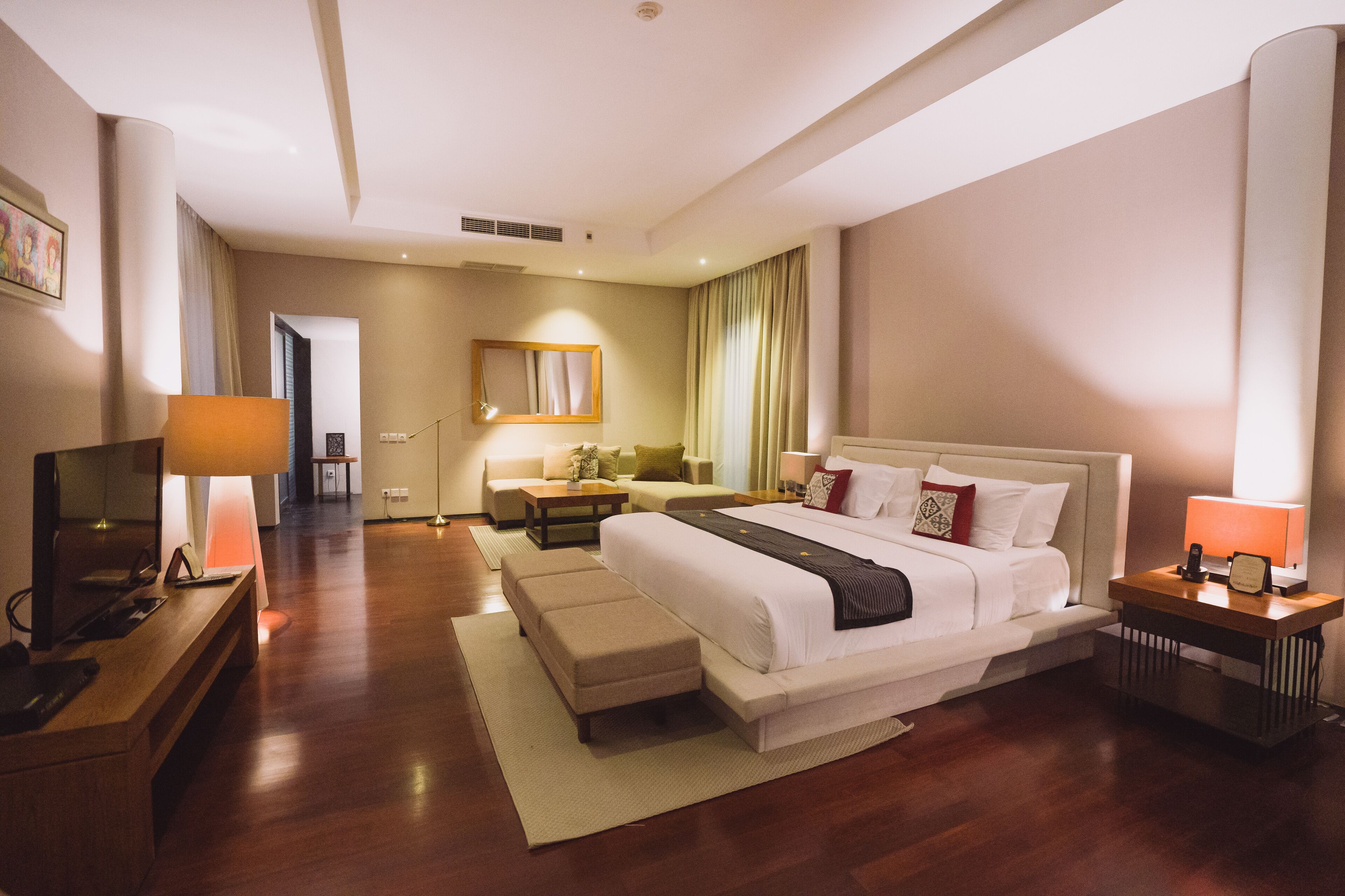 A modern hotel room with a large bed, a TV, a desk, and a sofa.