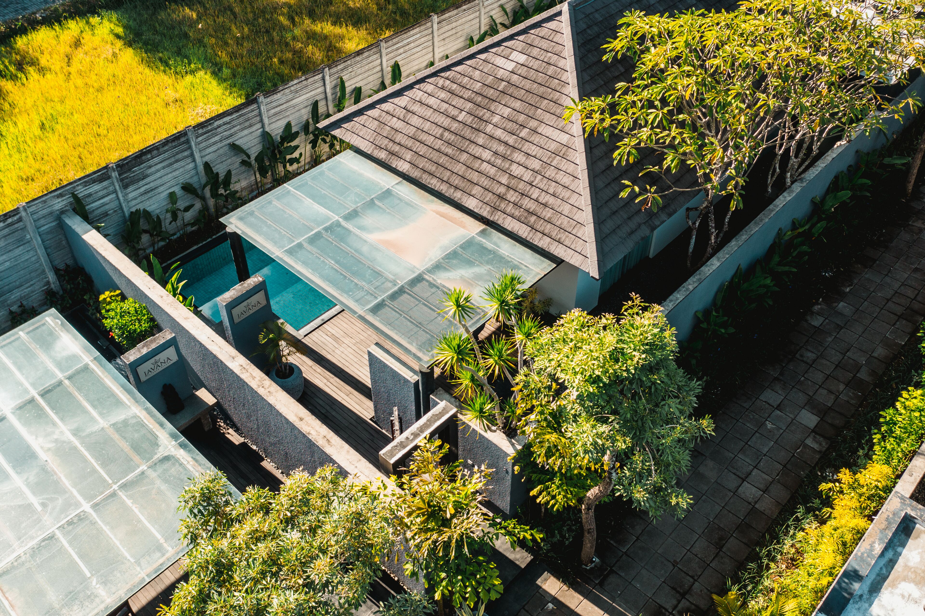 A rooftop pool with glass panels, surrounded by lush greenery and a wooden deck.