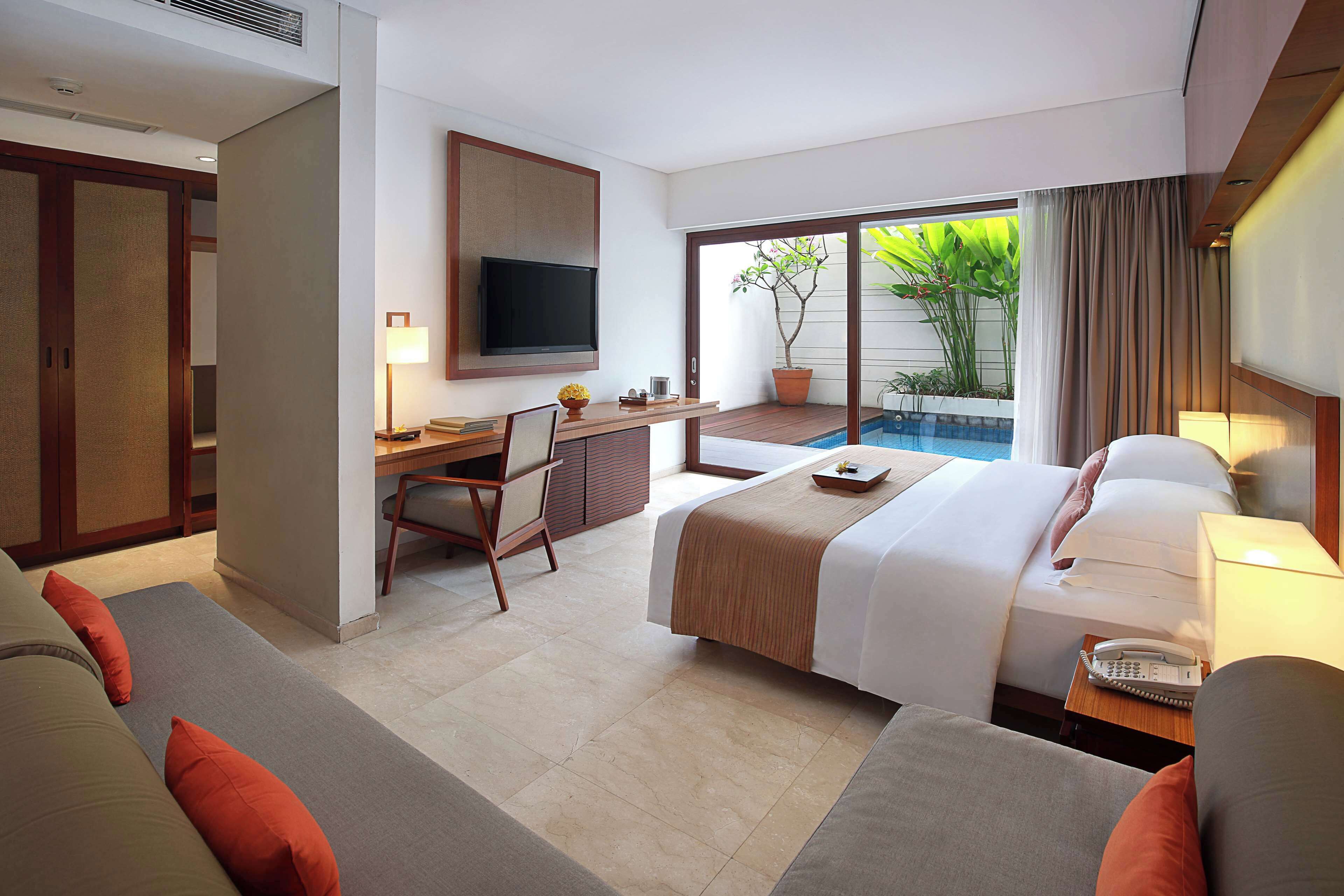 A hotel room with a bed, a desk, a television, and a view of a pool.
