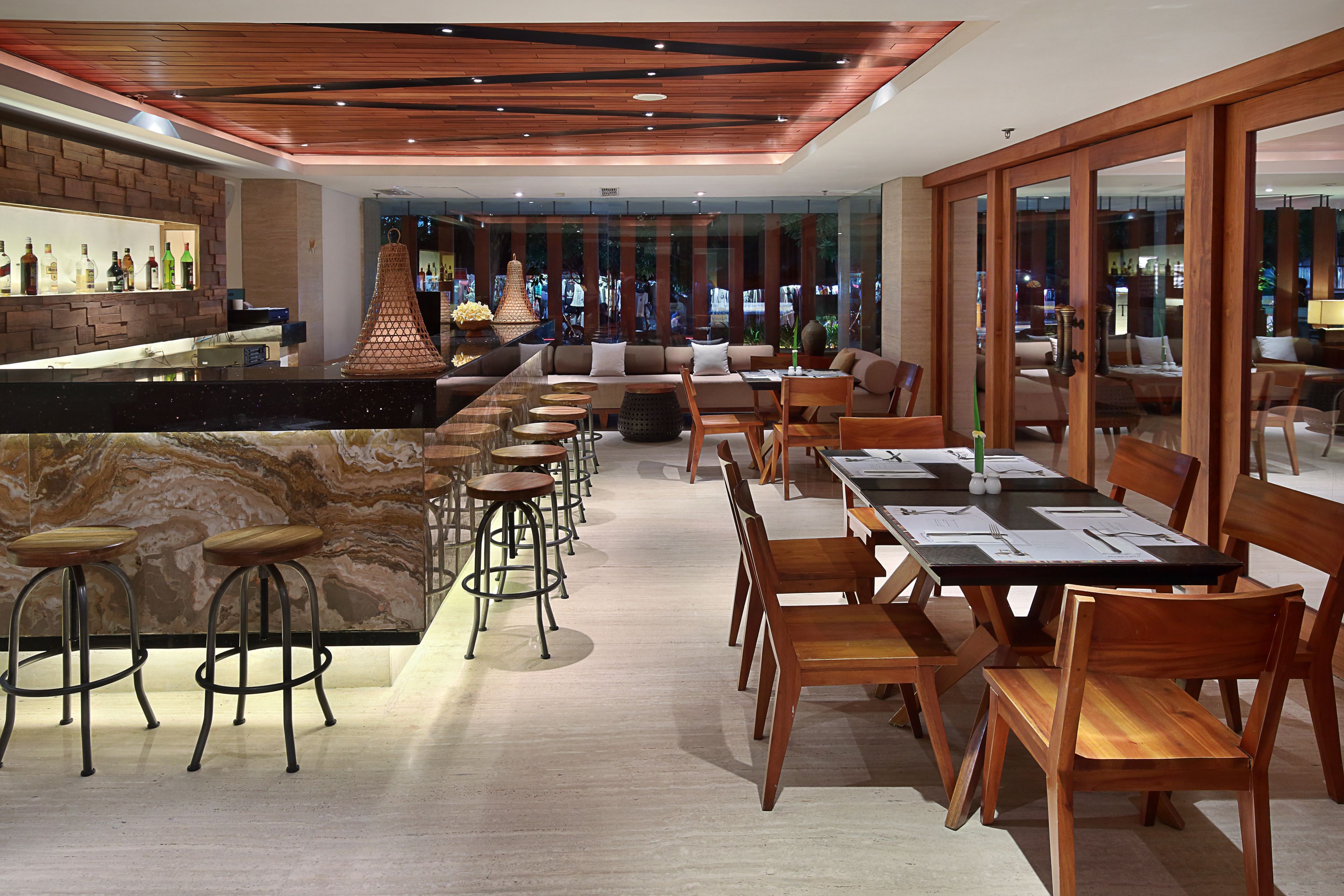 A modern bar area with a marble countertop, stools, and a seating area with wooden tables and chairs.