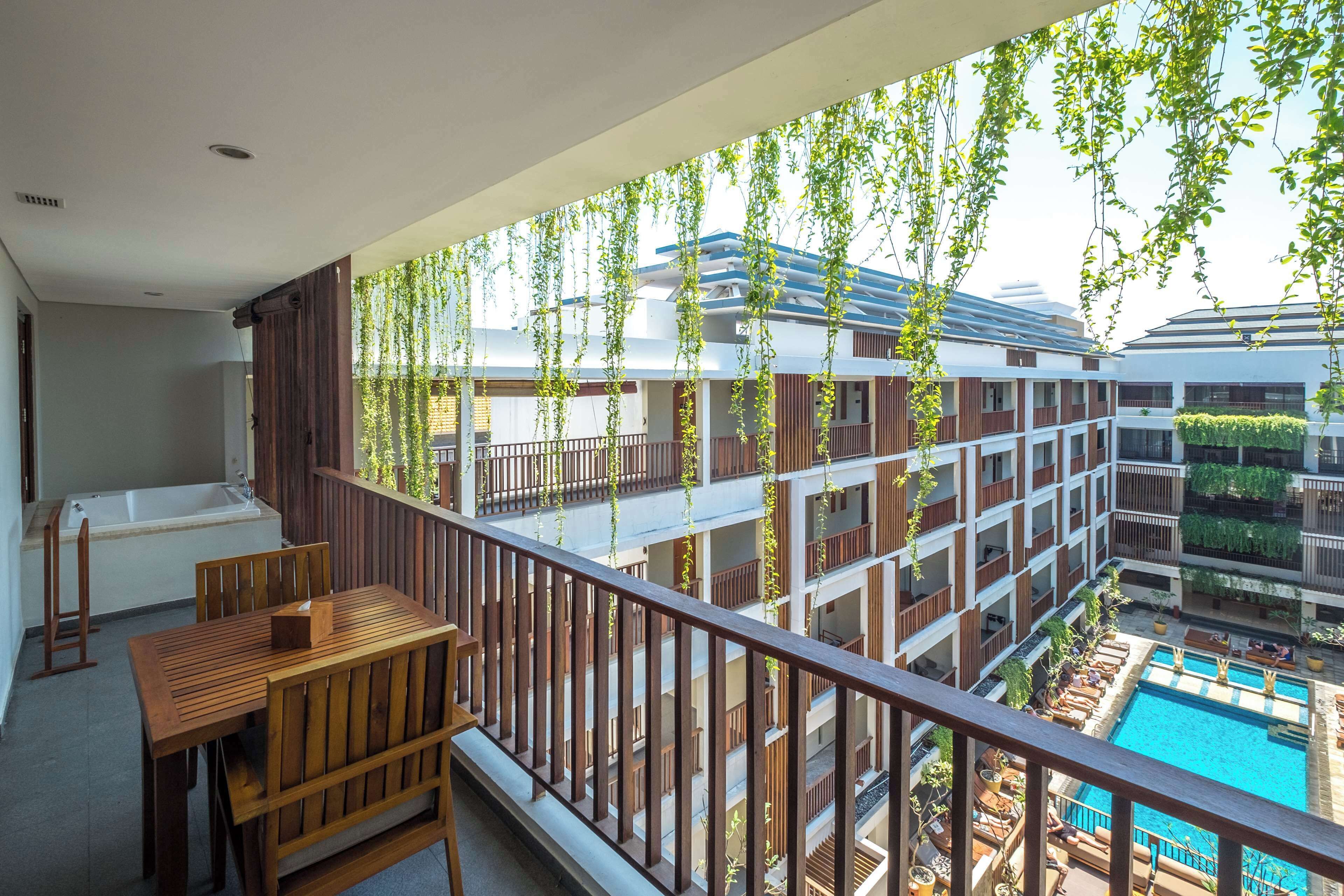 Ein Balkon mit Holztisch und Stühlen, der Blick auf einen Swimmingpool und ein mehrgeschossiges Gebäude mit Balkonen freigibt.