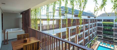 A balcony with a wooden table and chairs, overlooking a swimming pool and a multi-story building with balconies.