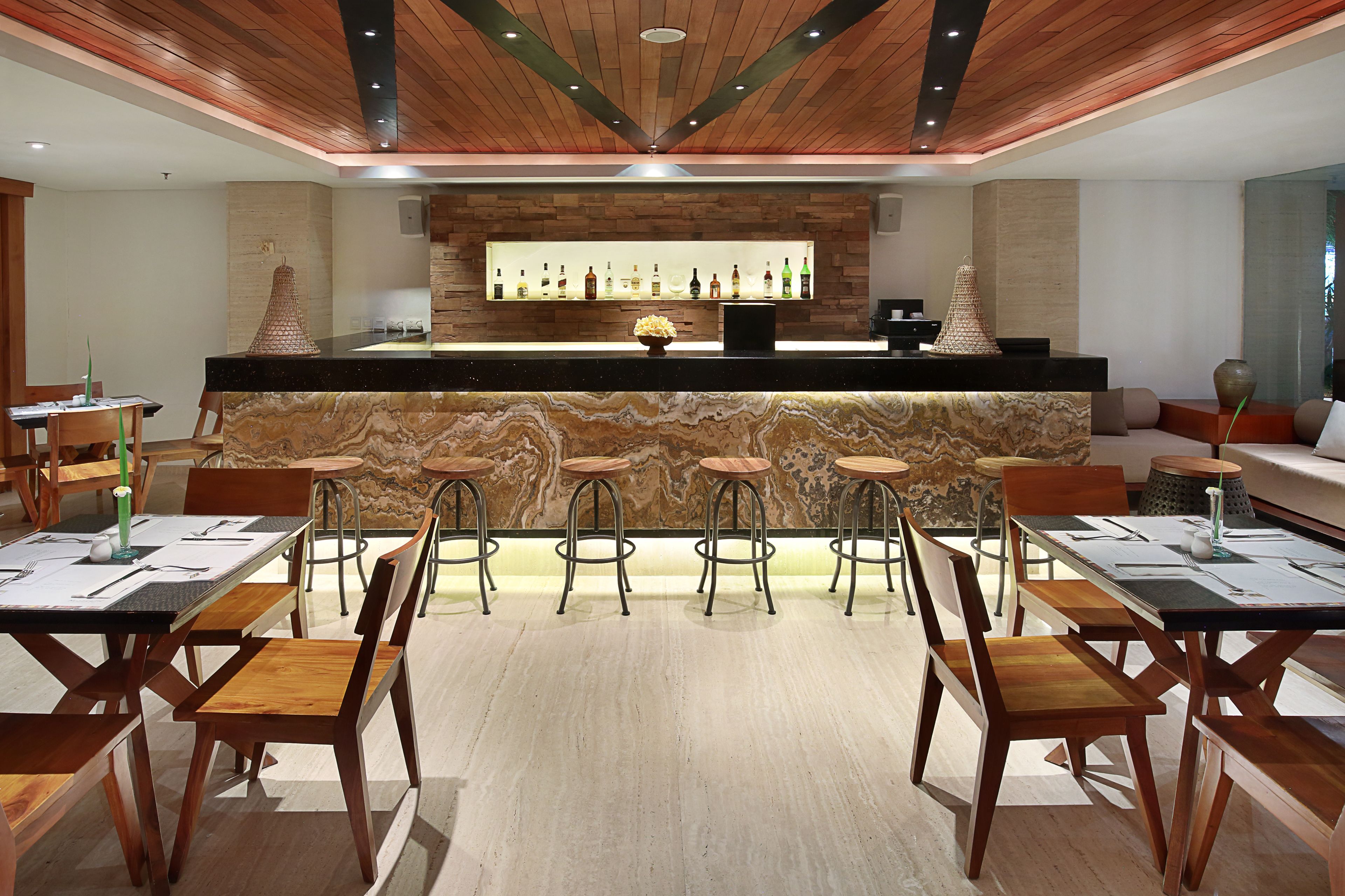 A modern bar area with a marble countertop, wooden bar stools, and a variety of bottles.