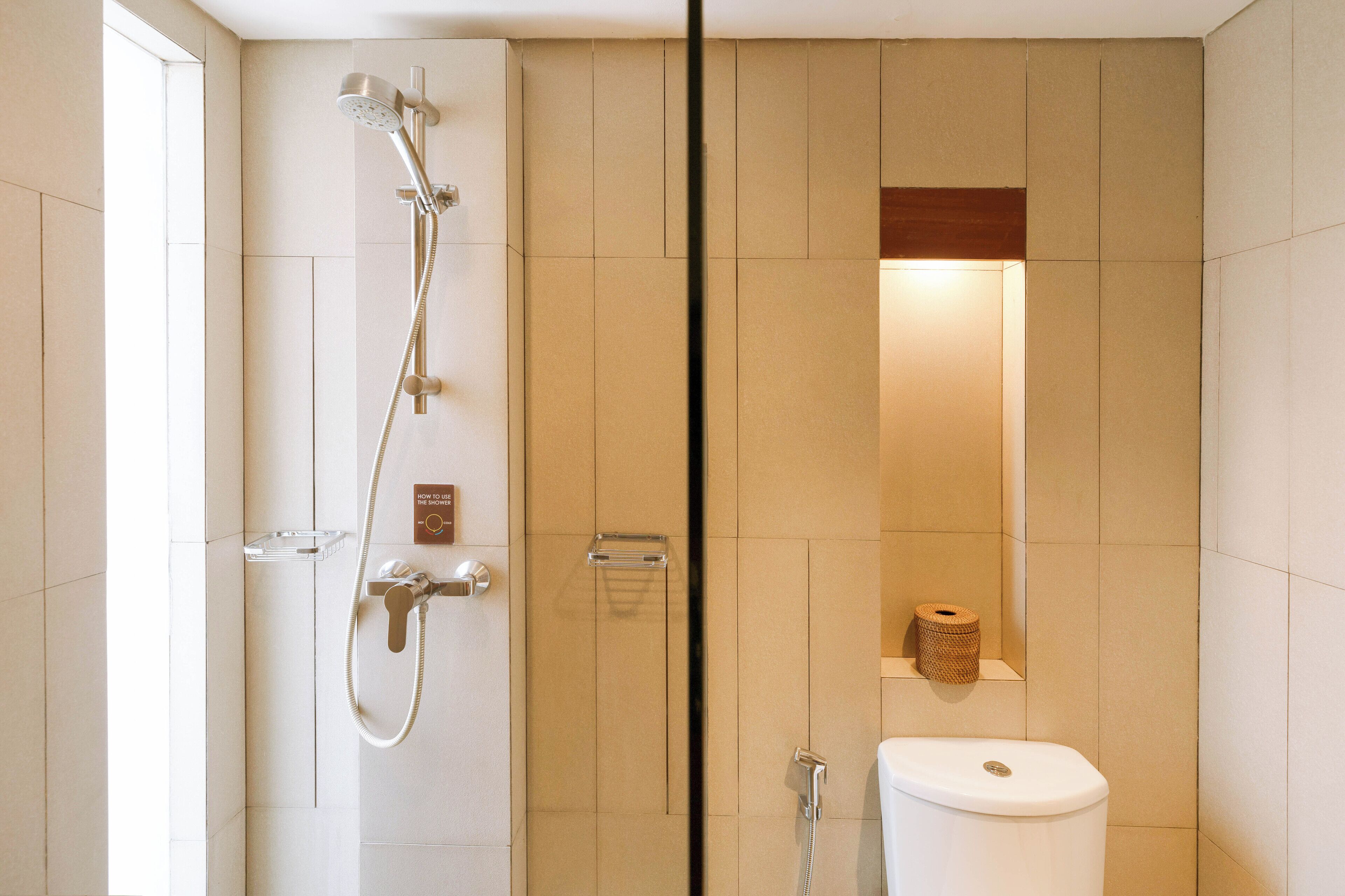 A modern bathroom with a glass-enclosed shower, a toilet, and a small shelf with a roll of toilet paper.