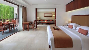 Quarto de hotel com cama grande, sofá, área de refeições e vista para o verde lá fora.