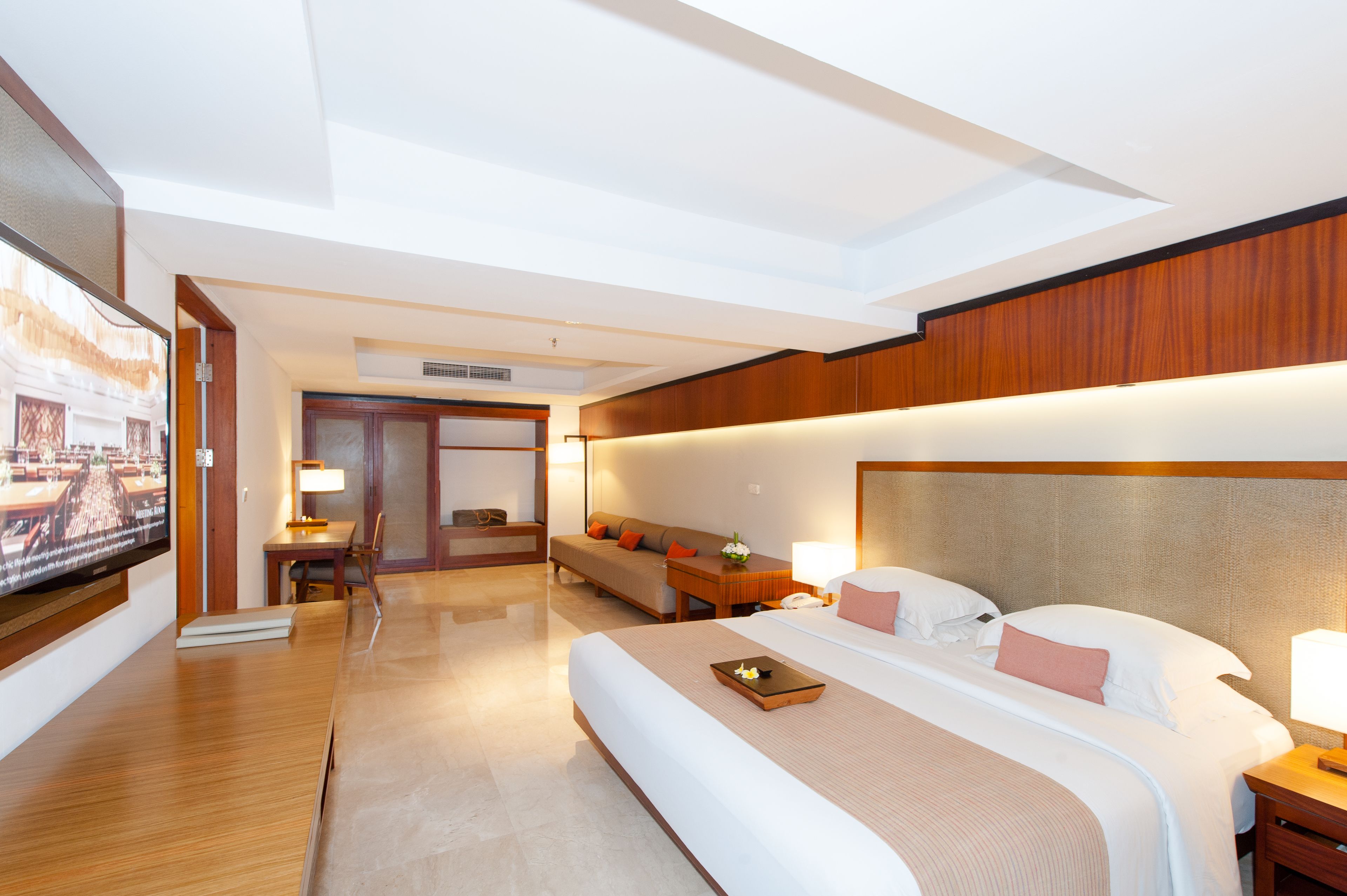 A hotel room with a large bed, a desk, a sofa, and a television.