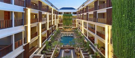 A multi-level hotel atrium with a central pool, balconies, and indoor plants.