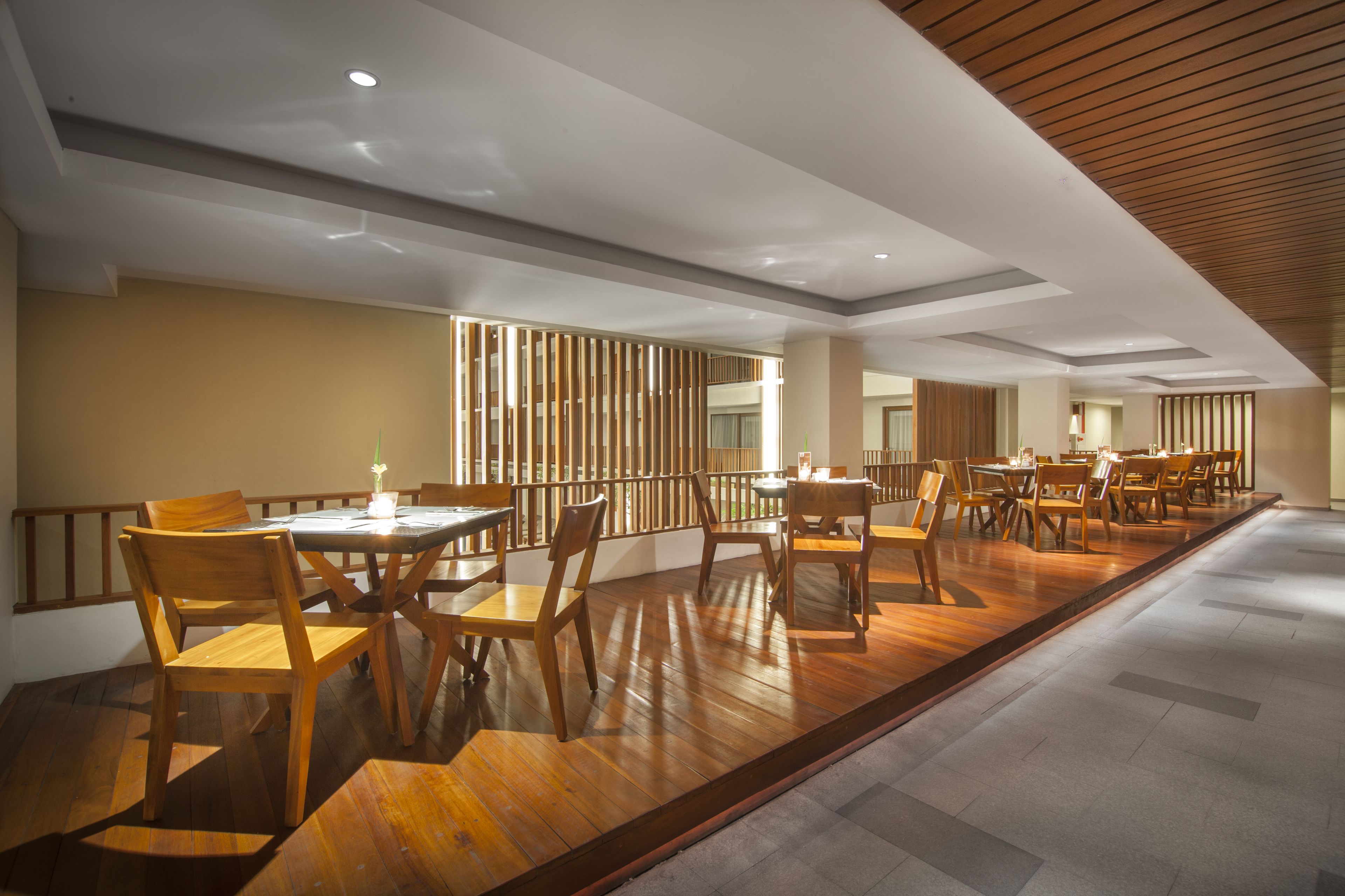 A spacious dining area with multiple wooden tables and chairs, a wooden ceiling, and a view of the outdoors.